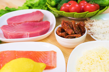 Raw appetizing fillet of tuna on a table with a yard of Greek salad with salmon and lemon cucumbers and tomatoes as well as cheese. The concept of a delicious and healthy home-made meal