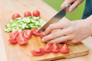 Close-up Delicate female hands cut a large knife with tomatoes on a quarter on a wooden board at home. Home kitchen. Healthy eating. The concept of vegetarianism