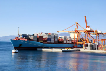 Fototapeta premium Container ship for carriage of goods with containers to shore in port ship port on horizon / Cargo transportation by sea and goods unloading process / Business logistics and transportation concept.