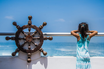 Girl observing the sea from a balcony of a house on the beach with a pirate ship helm at her side
