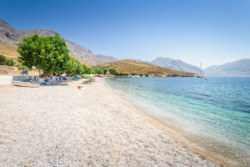 Fototapeta na wymiar Beautiful sunny holiday coast view to the greek blue sea with crystal clear water beach relaxing with some boats fishing cruising surrounded by hills mountains, Patmos, Kos Island, Dodecanese, Greece