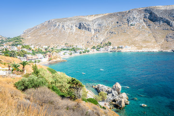 Beautiful sunny coast view to the greek blue sea with crystal clear water beach with some boats fishing cruising surrounded by hills mountains, Kantouni, Patmos, Kos, Dodecanese Islands, Greece 