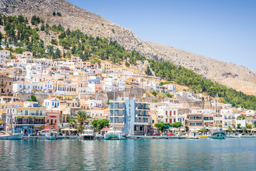 Fototapeta na wymiar Beautiful sunny coast view to the greek blue sea with crystal clear water to the traditional town of Pothia surrounded by hills mountains with boats in harbor, Kalymnos Island, Kos, Dodecanese Greece