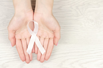 Oncological disease concept. Hands holding white ribbon as a symbol of lung cancer on wooden...