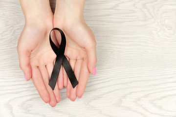 Oncological disease concept. Hands holding black ribbon as a symbol of melanoma.