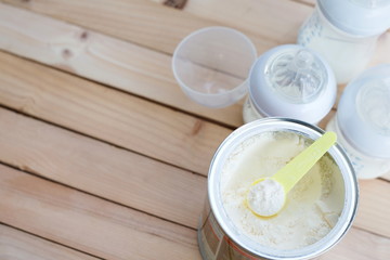 Milk powder for baby in measuring spoon in can and milk bottle on wooden table with copy space.