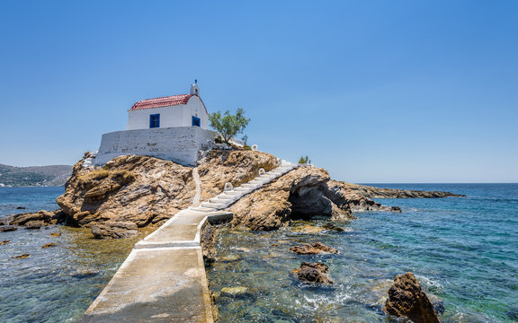 Holy white and blue chruch of agios Isidoros shining at an empty place in the greek sea only reachable by a stone boardwalk over the water on the island of Leros, Dodecanese, Greece