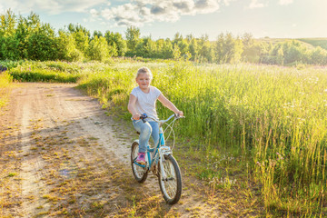 Obraz premium Happy child riding bike. Young girl on bicycle in sunny summer park. Healthy school children summer activity. Kids playing and cycling outdoors. Little girl learns to keep balance while riding bicycle