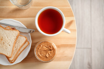 Jar of creamy peanut butter with bread and cup of tea on table