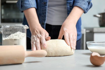 Woman kneading dough near graduated jug with flour on table in kitchen