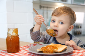 Little boy eating jam at table in kitchen