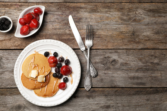 Delicious pancakes with berries, honey and butter served for breakfast on table