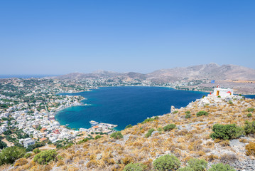 Fototapeta na wymiar Beautiful sunny greek white church and village town Agia Marina harbor view to the greek blue sea water from the old castle surrounded mountains, Medieval Castle, Leros, Dodecanese Islands, Greece 