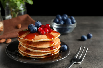 Stack of tasty pancakes with berries and syrup on table