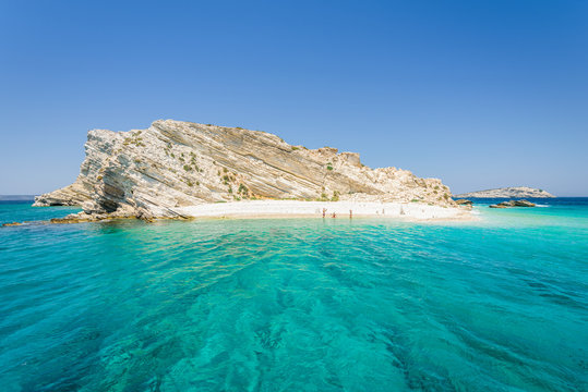 Beautiful sunny coast view to a small greek island and crystal clear blue water beach with some boats cruising and people swimming, White Island, Aspronisi, Leros, Dodecanese/ Greece &ndash; July 22 2017