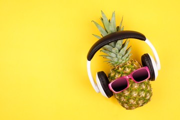 Hipster pineapple with sunglasses and headphones. Top view against a yellow background. Minimal...