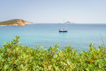 Plakat Peaceful sunny coast view to a empty greek holiday bay with crystal clear blue water sandy beach for sunbathing and some boats cruising fishing in background