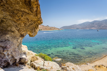 Beautiful sunny view through a rocky cave to the greek blue sea with crystal clear water from an a hill with boats cruising fishing surrounded by mountains, Patmos Island, Kos, Dodecanese/ Greece 
