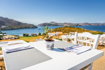 Fototapeta premium Your table is already reserved at the greek mediterranean sea behind crystal clear blue water and a beautiful coastal aegean bay with fishermen boats cruising, Patmos Island, Kos, Dodecanese, Greece