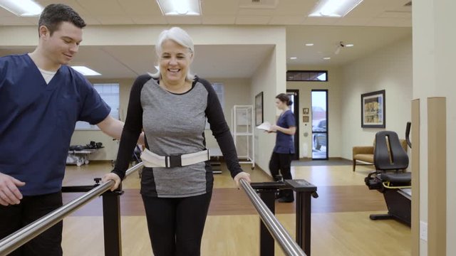 Medium shot of a senior woman walking in parallel bars