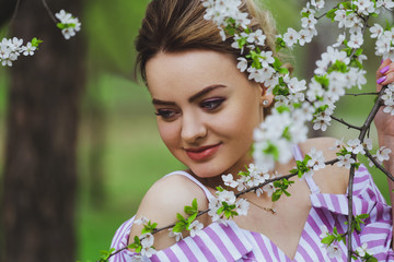 Fototapeta premium Beautiful blonde girl with blond hair in a dress on a background of spring blooming trees