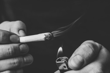 joint in hand. A man smokes cannabis weed, a . Smoke on a black background. Concepts of medical marijuana use and legalization of the cannabis.Black and white