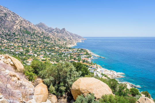 Beautiful sunny greek village town church and harbor view to the blue sea with crystal clear water and fishing boats cruising yacht at shore, Ikaria Island, Karkinagri, Sporades/ Greece &ndash; 08 01 2017