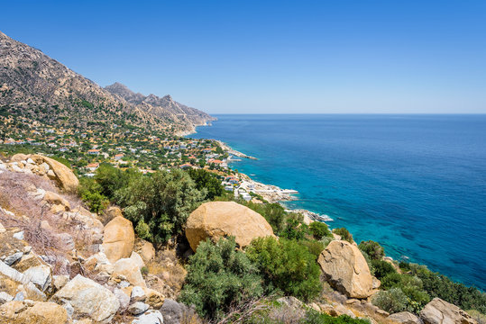 Beautiful sunny greek village town church and harbor view to the blue sea with crystal clear water and fishing boats cruising yacht at shore, Ikaria Island, Karkinagri, Sporades/ Greece &ndash; 08 01 2017