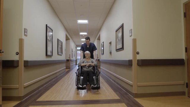 Steadicam shot of a male nurse pushing an old woman in a wheelchair