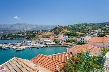 Fototapeta premium Beautiful sunny greek village town white house and harbor view to the aegean blue sea with crystal clear water and fishing boats cruising yacht white houses, Ikaria Island, Evdilos, Sporade, Greece
