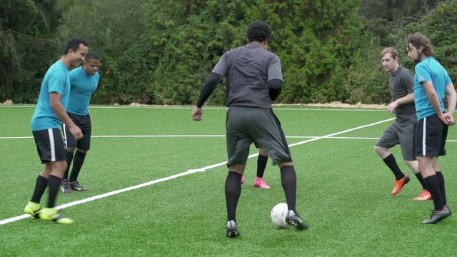 Male soccer players standing in circle passing ball.