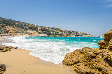 Fototapeta na wymiar Beautiful sunny coast view to cozy holiday bay with crystal clear blue water sandy beach for sunbathing and heavy huge waves surfing from the greek sea, Ikaria Island, Armenistis, Greece - 08 04 2017