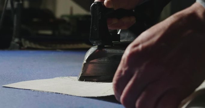An old tailor iron the tailored shirt before folding it and sending it to the buyer. Concept of: tailoring, tradition, precision.