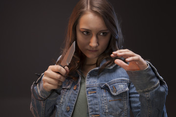 Teen girl with a knife in hand, ready to defend herself against an attacker.  Studio shoot on dark...
