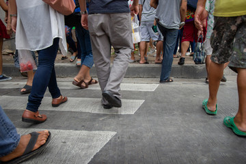 People walk across the street across the crosswalk. Selective focus on feet of people.