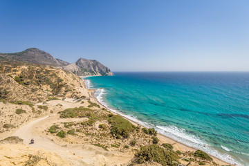 Fototapeta premium Beautiful sunny coast view to the greek mediterranean blue sea with crystal clear water and pure sandy beach empty place with some mountains rocks surrounded, Kos, Dodecanese Islands, Greece