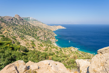 Fototapeta na wymiar Beautiful sunny coast view to the greek mediterranean blue sea with crystal clear water and pure sandy beach empty place with some mountains rocks surrounded, Kos, Dodecanese Islands, Greece