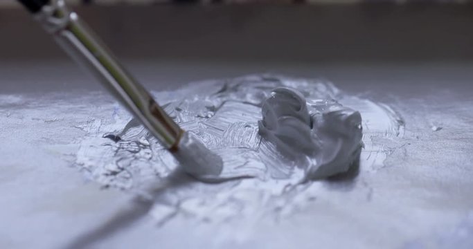 ECU detail artist dips fine sable brush into a a blob of mixed pale gray oil paint ready for painting. Hand-held 4K recorded in slow motion at 60fps.
