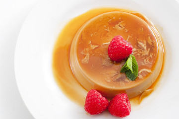 Homemade dessert and smooth custard sweets concept with top view of creme caramel, flan, or caramel pudding covered in sweet syrup and raspberries isolated on white background with copy space