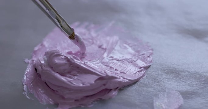 ECU detail artist dips fine sable brush into a a blob of mixed pink oil paint ready for painting. Hand-held 4K recorded in slow motion at 60fps.