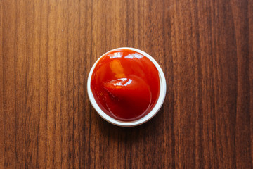 A cup of ketchup place on wooden table.