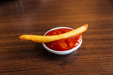 French fried dipping in ketchup the place on wooden table.
