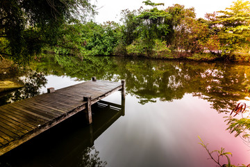 Long exposure of pier in calm lake, with nature all around, water is silky smooth, colored light leaks on the sides