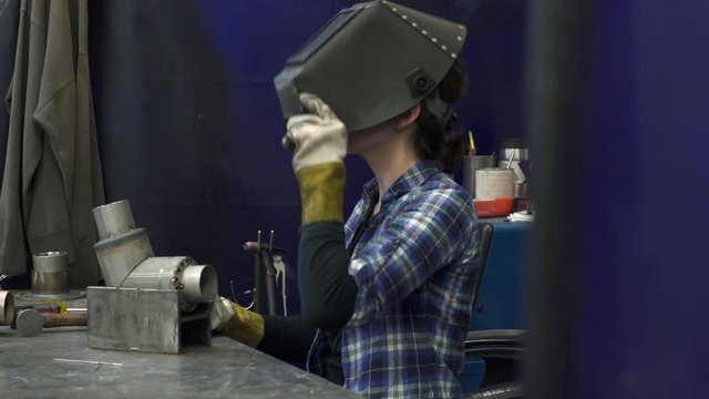 Young woman starting welding a pipe in a factory