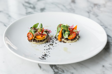 Quinoa canapes topping with pan seared asparagus, tomato and baby vegetables and olive oil served on white plate.