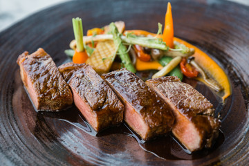 Roasted medium rare wagyu beef served with sour sauce with roasted baby vegetables on stone plate.