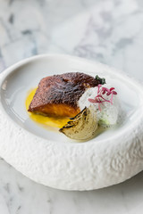 Pan seared trout. served with yellow sauce, foam amd roasted sliced onion on curved white plate. 