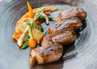 Roasted medium rare wagyu beef served with sour sauce with roasted baby vegetables on stone plate.