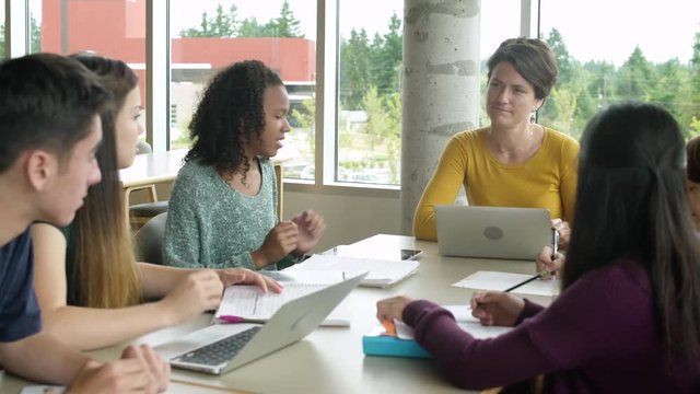 Female teacher talking to students while sitting together at a table