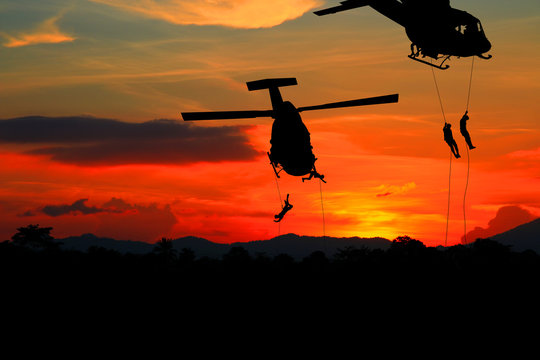 Silhouette Soldiers rappel down to attack from helicopter with sunset and copy space add text ( Concept stop hostilities To peace)